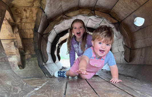 Two children smiling crawling through a tunnel wearing preloved clothing