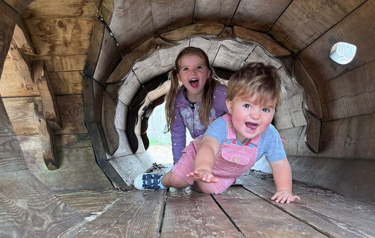 Two children smiling crawling through a tunnel wearing preloved clothing