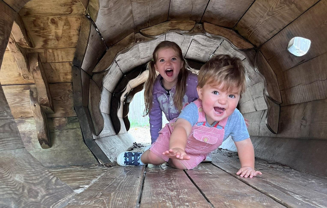 Two children smiling crawling through a tunnel wearing preloved clothing